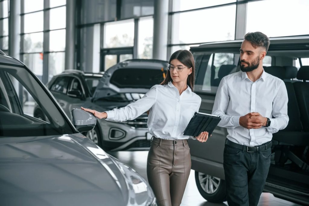 A female GMC SUV service representative shows a male prospective buyer a grey vehicle in the
