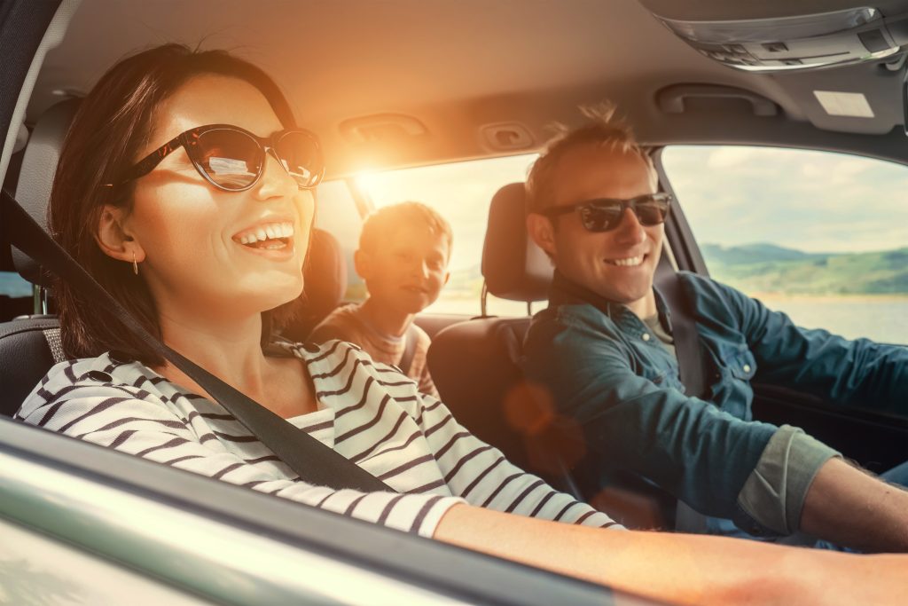 Mom dad and children laughing on a Summer Road Trip as the sun shines brightly through the GMC SUV window.